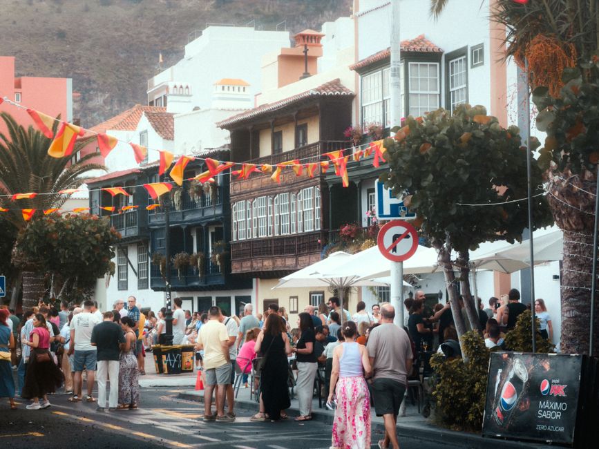 Multitudes disfrutando de un animado festival callejero en La Palma, España, con decoraciones coloridas y arquitectura histórica.