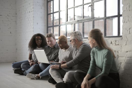 Concentrated serious diverse coworkers surfing laptop and working on project while sitting on floor and leaning on white brick wall