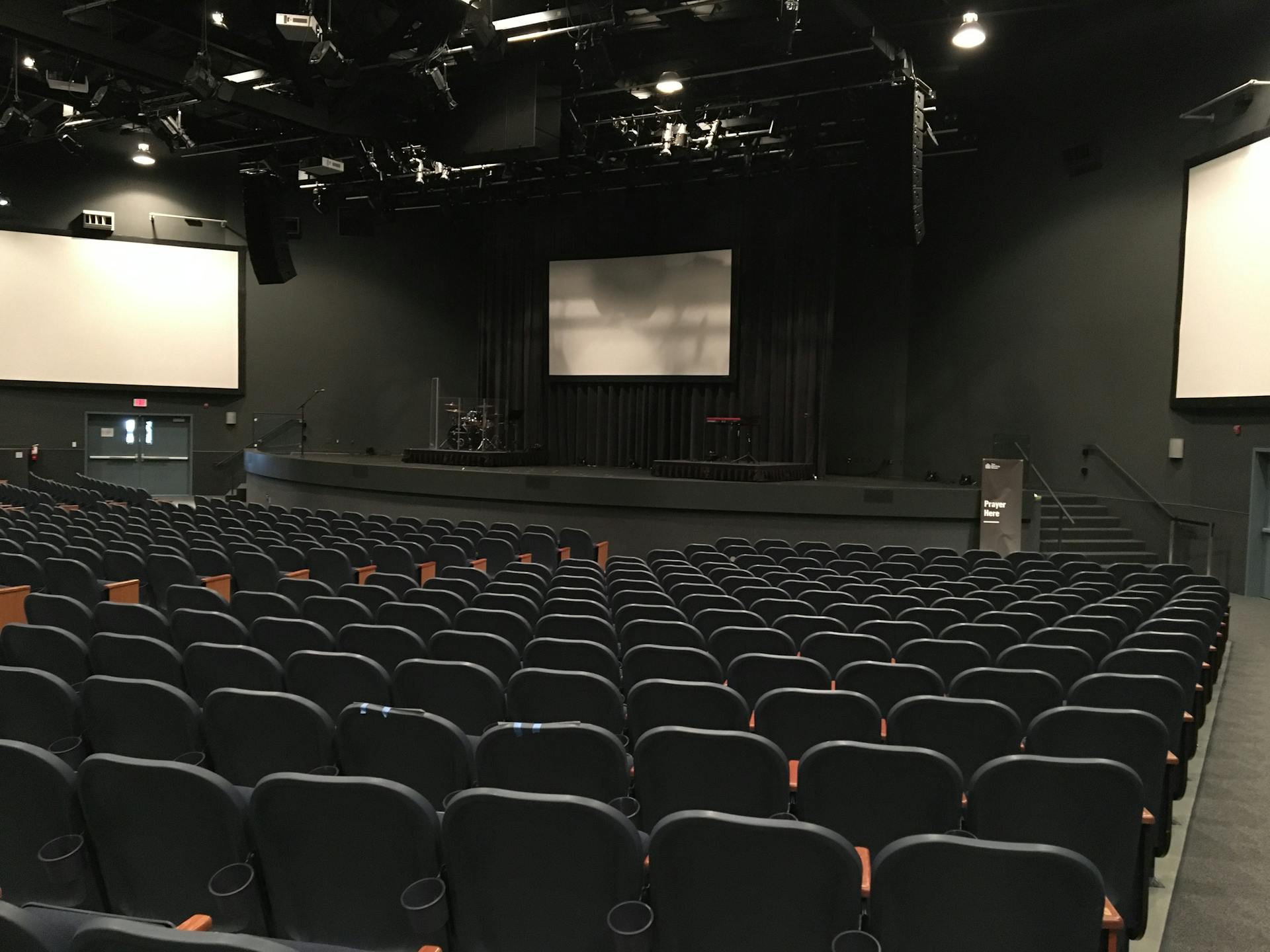 Rows of comfortable empty seats in modern theater hall with stage and screens