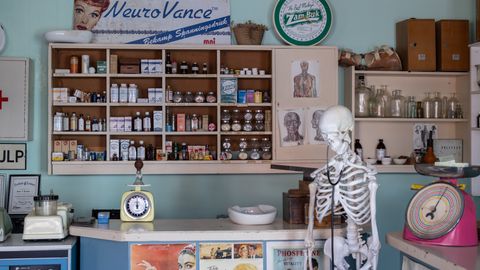 A nostalgic view inside an old-timey pharmacy featuring vintage medicine bottles and a medical skeleton on display.