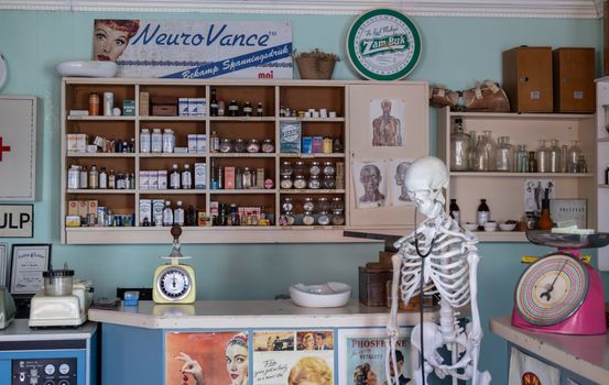 A nostalgic view inside an old-timey pharmacy featuring vintage medicine bottles and a medical skeleton on display.