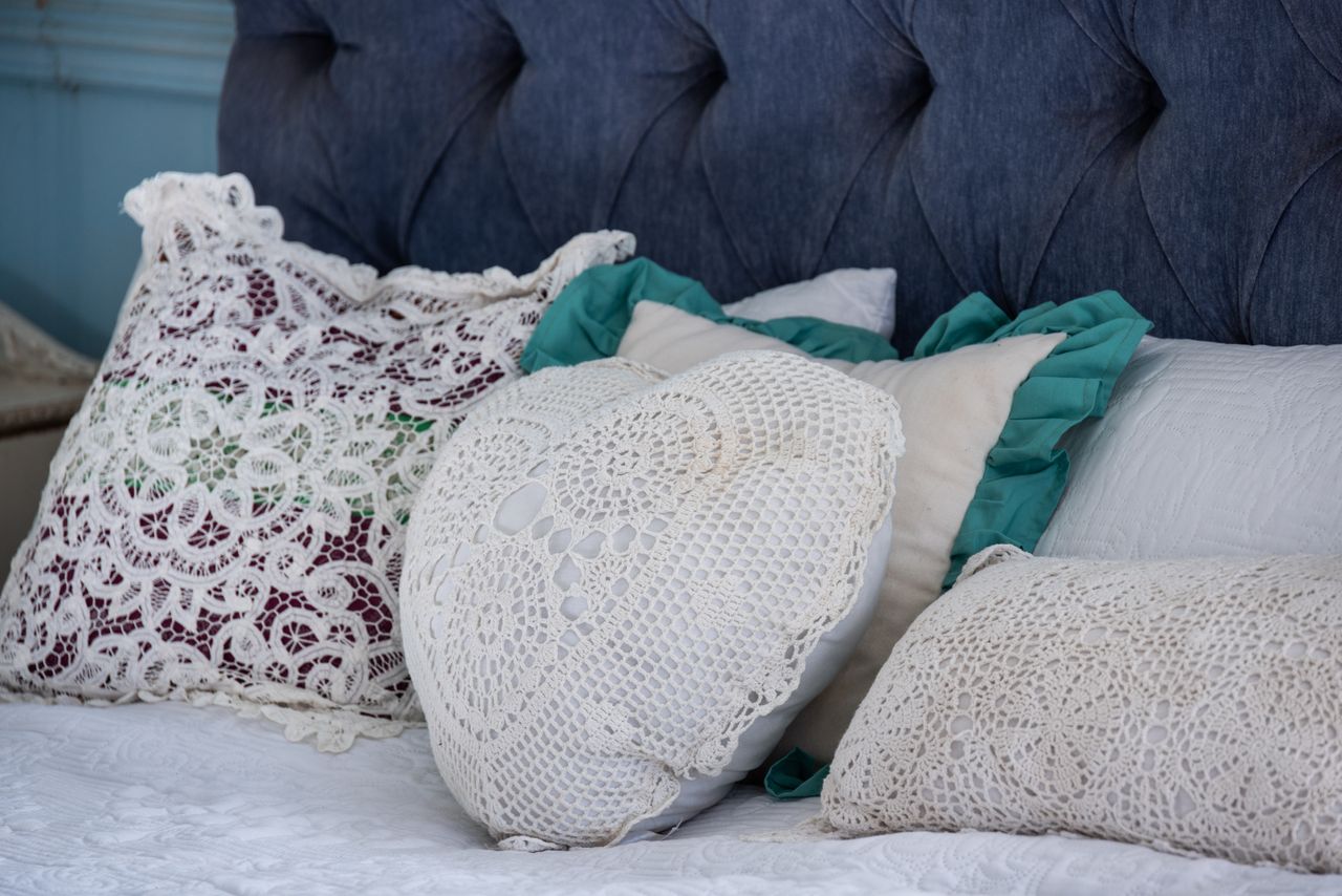 Decorative pillows with lace and ruffled flange edges arranged on a bed with a tufted headboard
