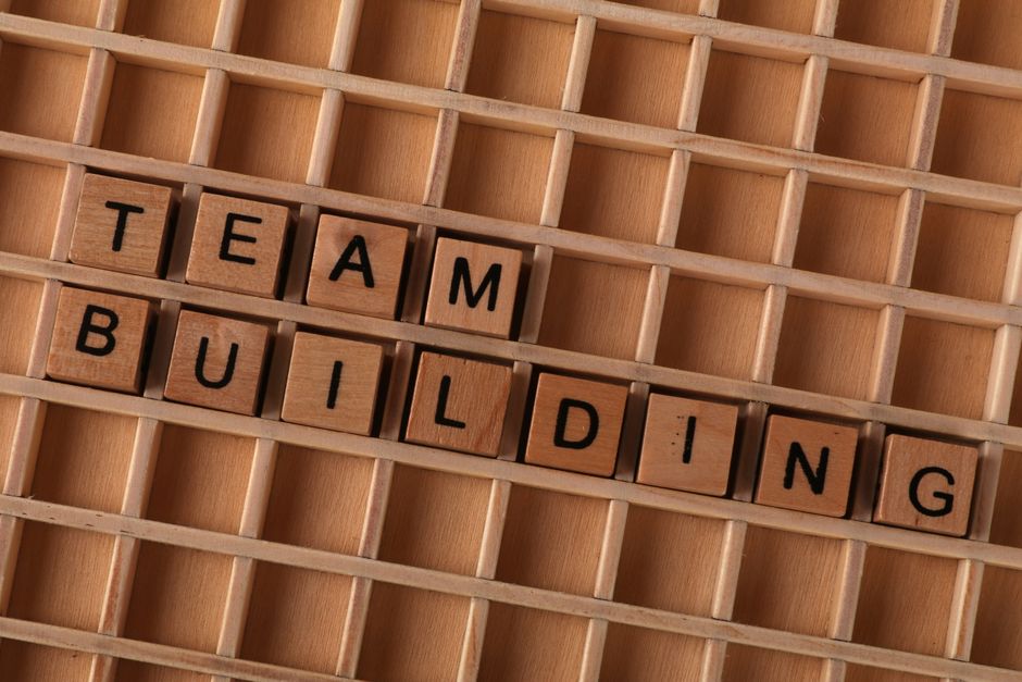 'Team Building'と綴られた木製の文字タイルがグリッド状の表面に配置され、コラボレーションを象徴しています。
