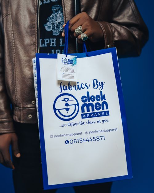 Free A man in a leather jacket holds a branded Sleek Men Apparel shopping bag. Stock Photo