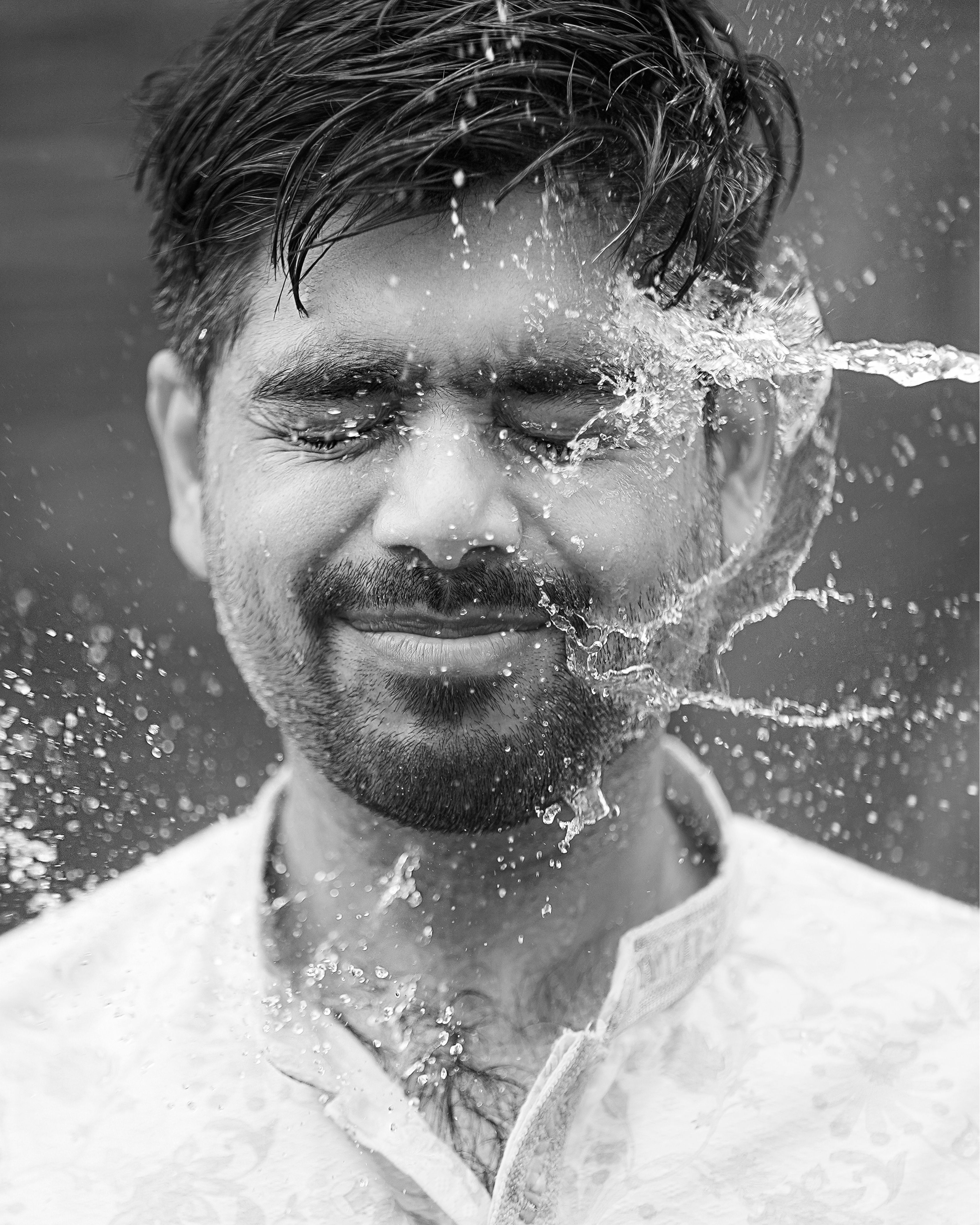 A man enjoying a splash of water on his face, captured in black and white.