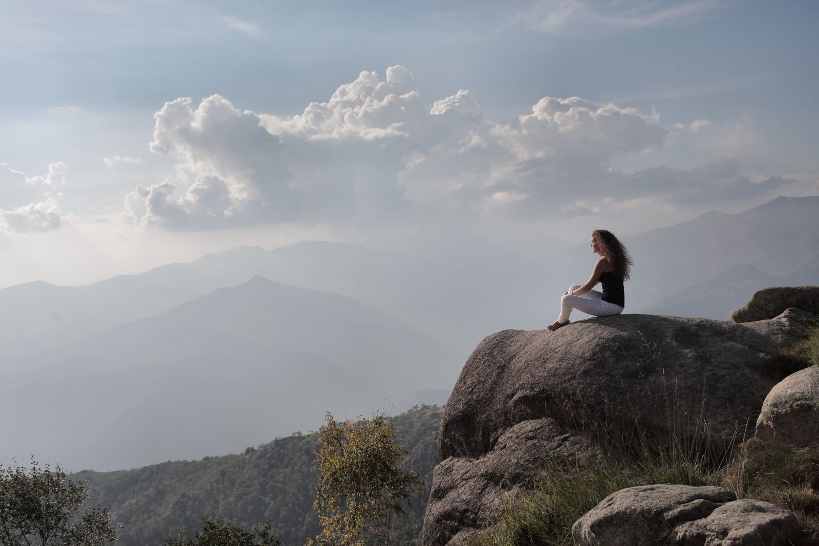 Woman sitting peacefully alone on a mountain rock, embodying the calm solitude of vairagya or non-attachment