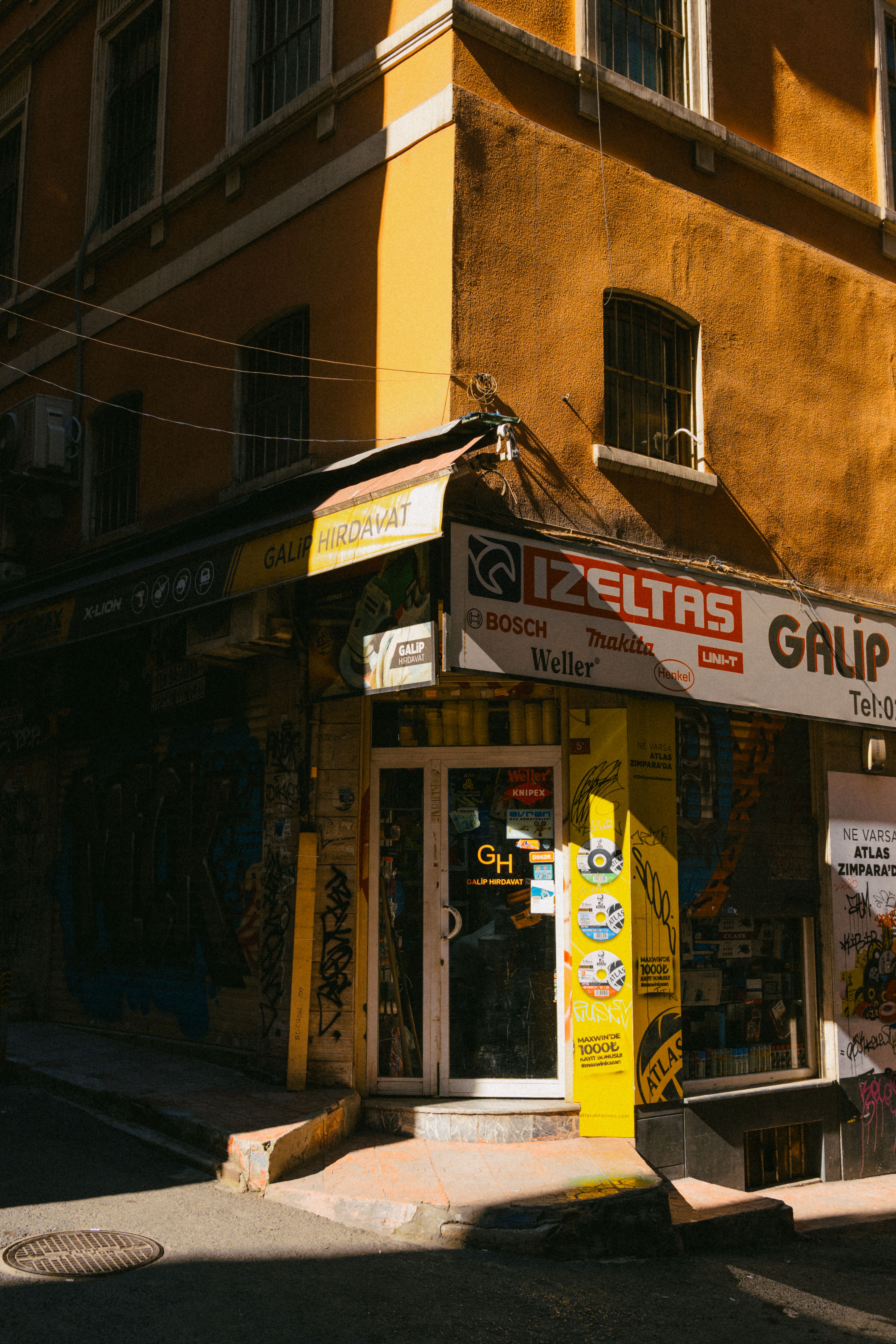 Yellow hardware shop in Istanbul's urban street with vibrant graffiti and harsh lighting.
