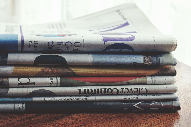 A stack of folded newspapers placed on a wooden table, symbolizing news and information.