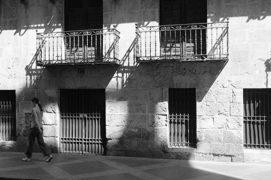 Una mujer pasa junto a un edificio histórico con balcones ornamentados en Alicante, España.