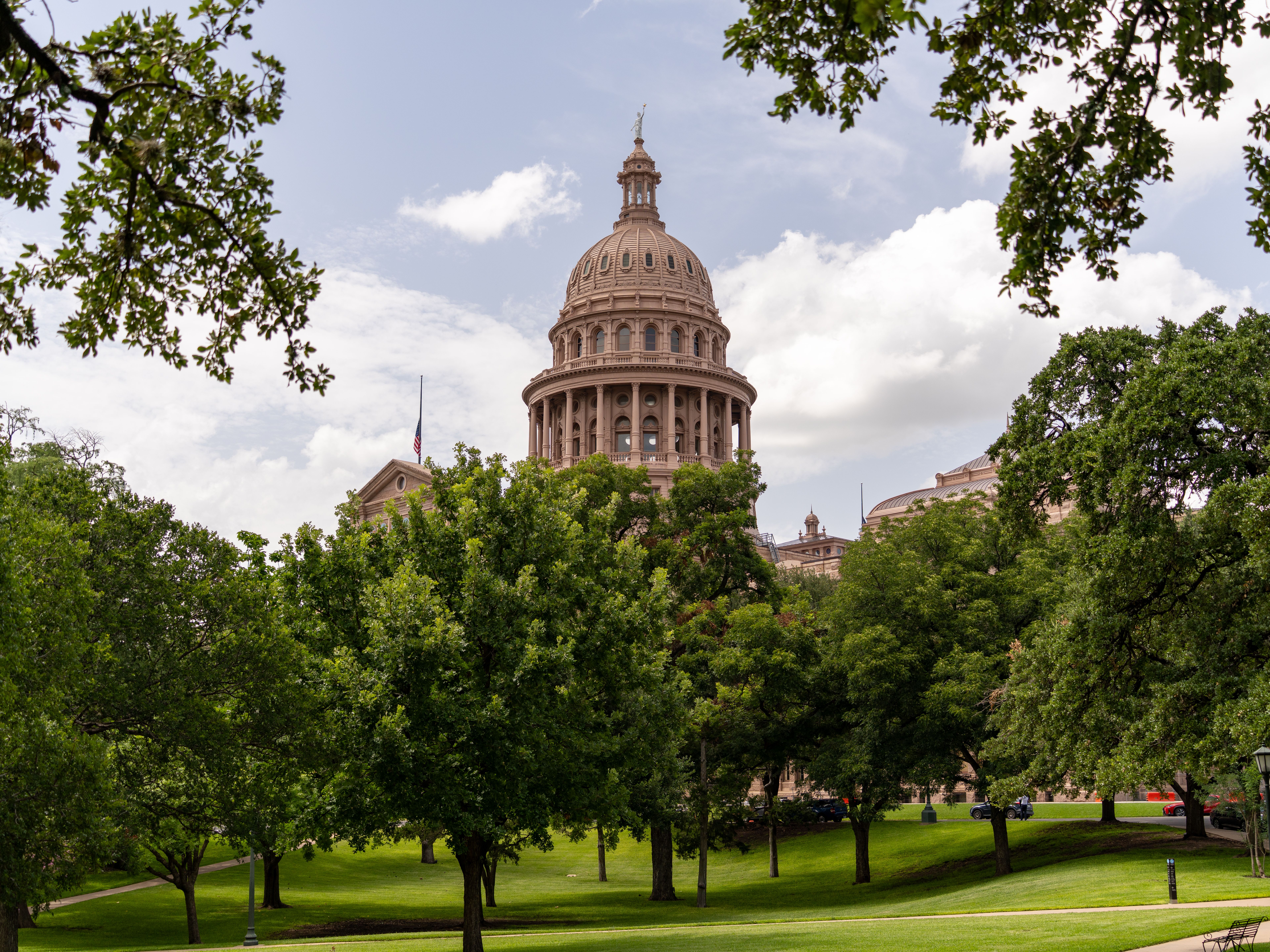 View of the Texas State Capitol dome amidst lush greenery on a sunny day in Austin.