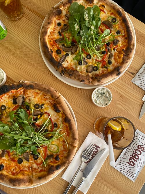 Free Top-down view of freshly baked pizzas topped with arugula and vegetables on a wooden table. Stock Photo