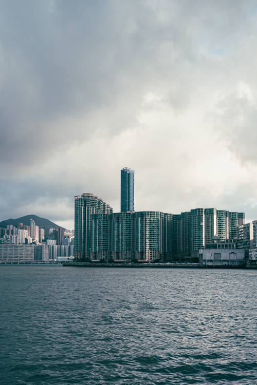 Free Dramatic view of Kowloon skyscrapers by the calm ocean under partly cloudy skies. Stock Photo