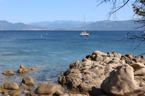Free Peaceful seaside view with rocky shoreline and sailboat on clear waters, perfect for travel inspiration. Stock Photo