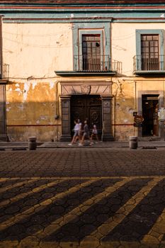 Three people walk past a vintage colonial building on a cobblestone street.