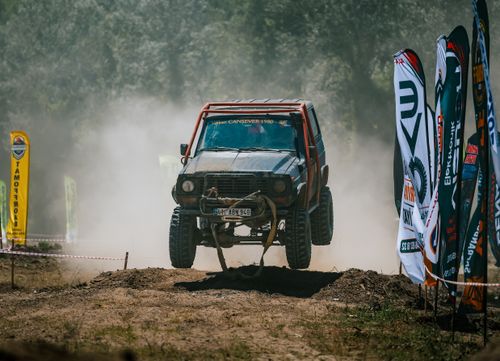 Free An off-road vehicle leaps over a rugged dirt track surrounded by promotional flags. Stock Photo