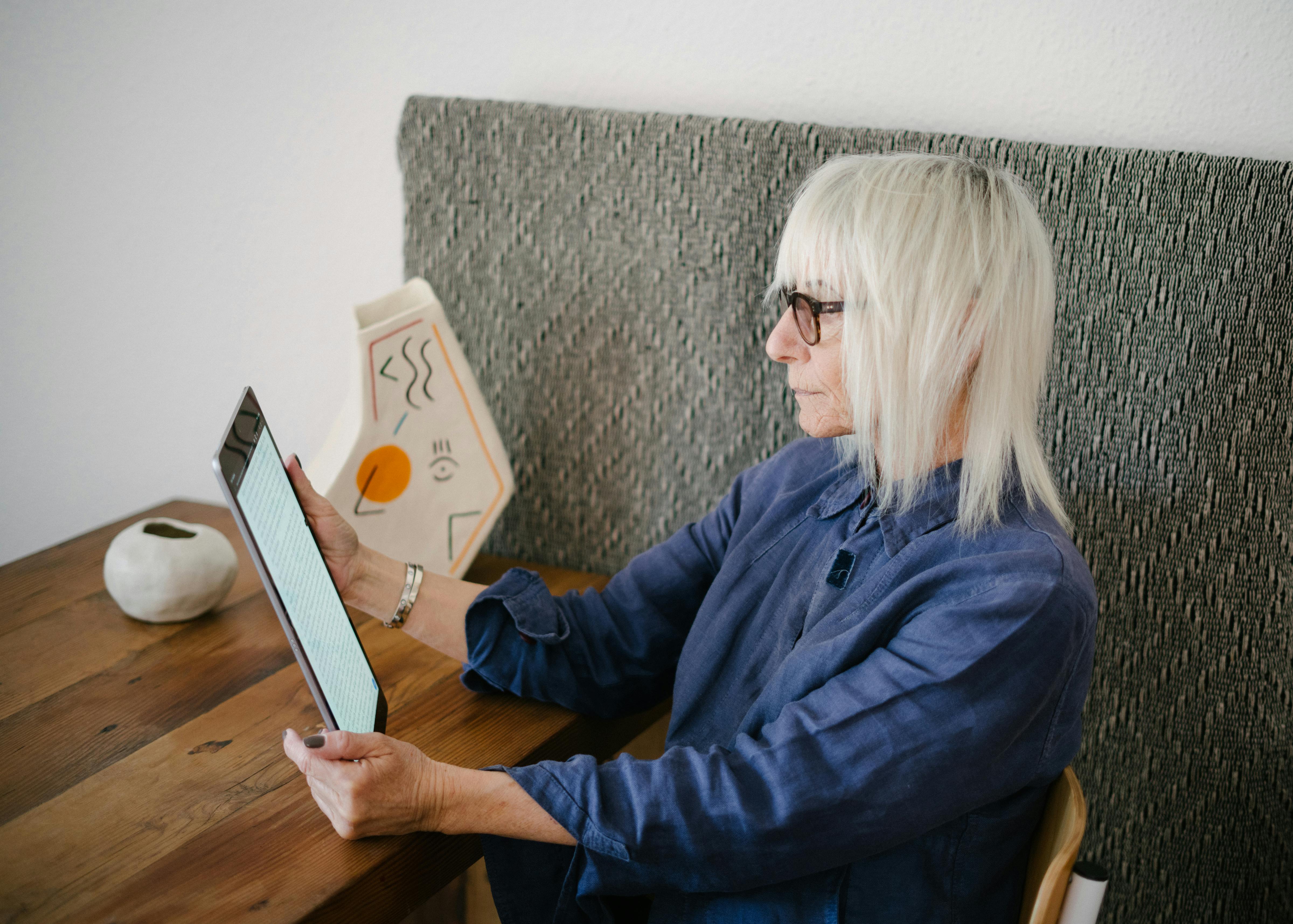 blond old woman reading book on tablet