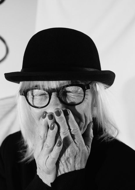 A candid grayscale portrait of a senior woman in a hat and eyeglasses, smiling.