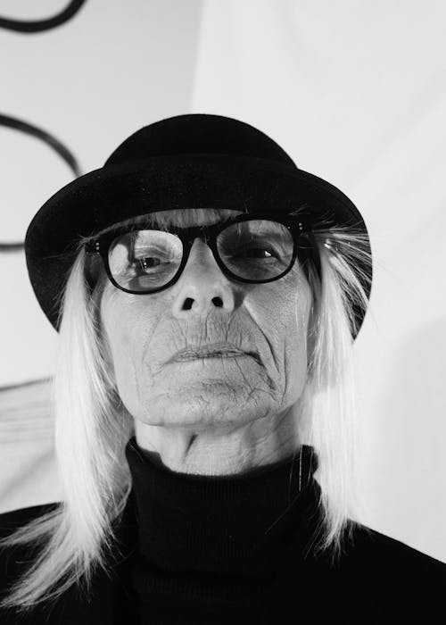 Senior stylish female with blond hair in eyeglasses hat and dark turtleneck looking at camera