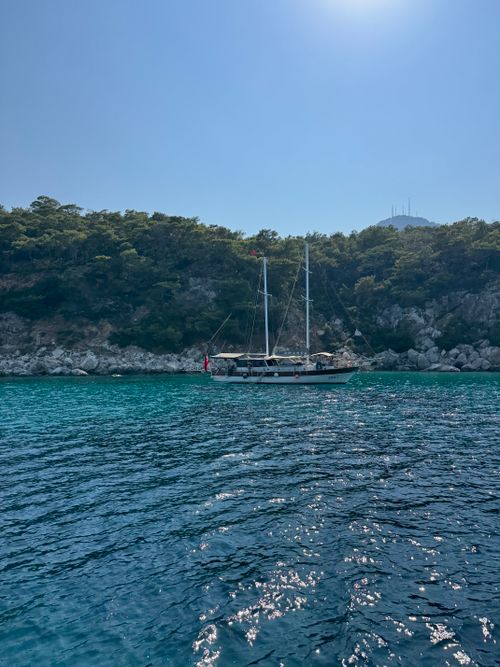 Free A serene day with a sailboat anchored near lush rocky cliffs under a clear blue sky. Stock Photo