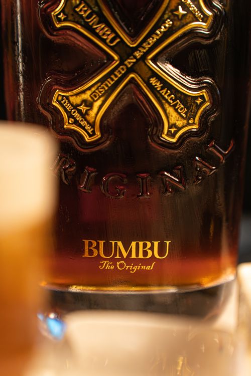 Free A detailed shot of a Bumbu rum bottle with its label and a blurred whiskey glass in the foreground. Stock Photo