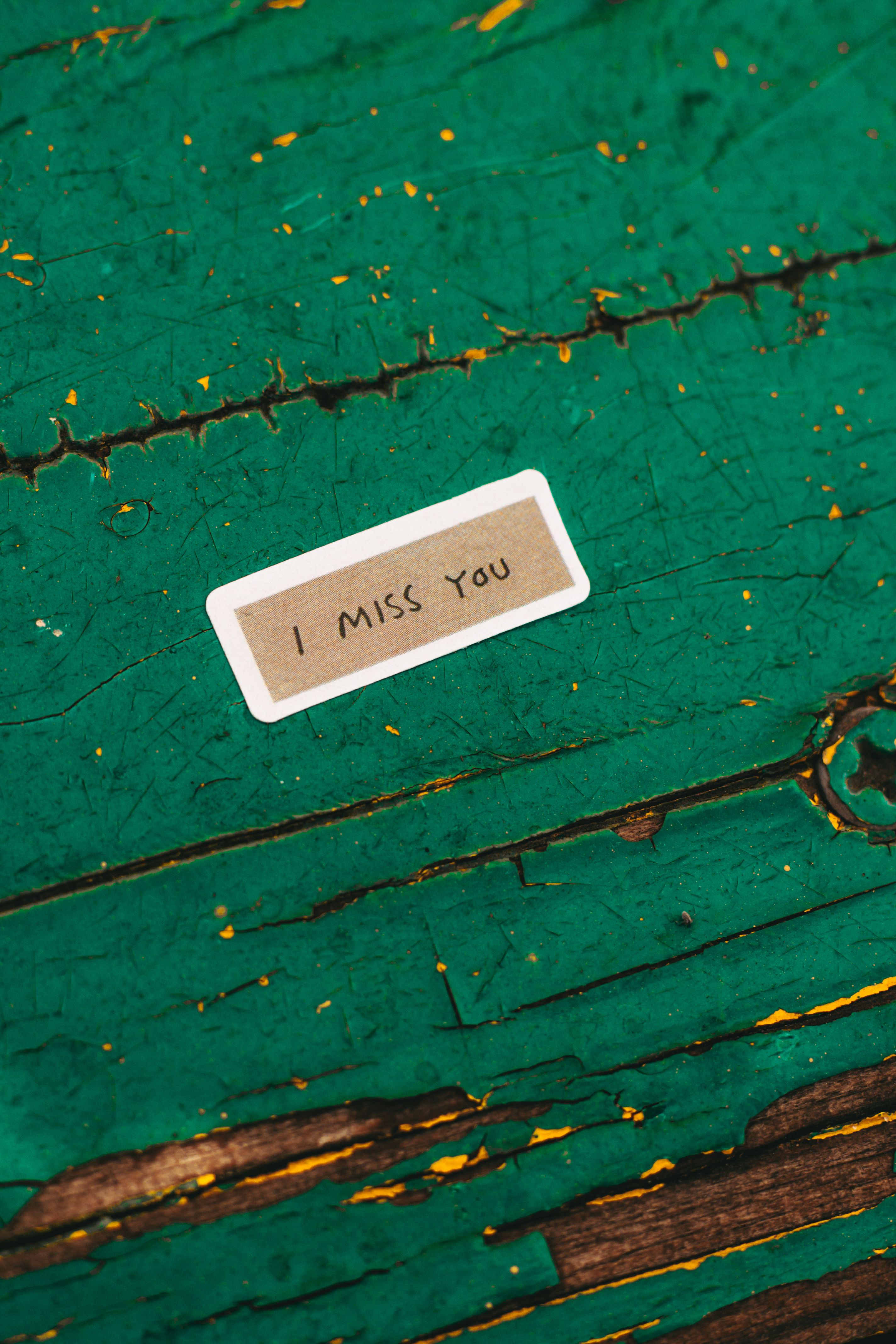 Small I miss you note on aged green wooden surface, evoking nostalgia.