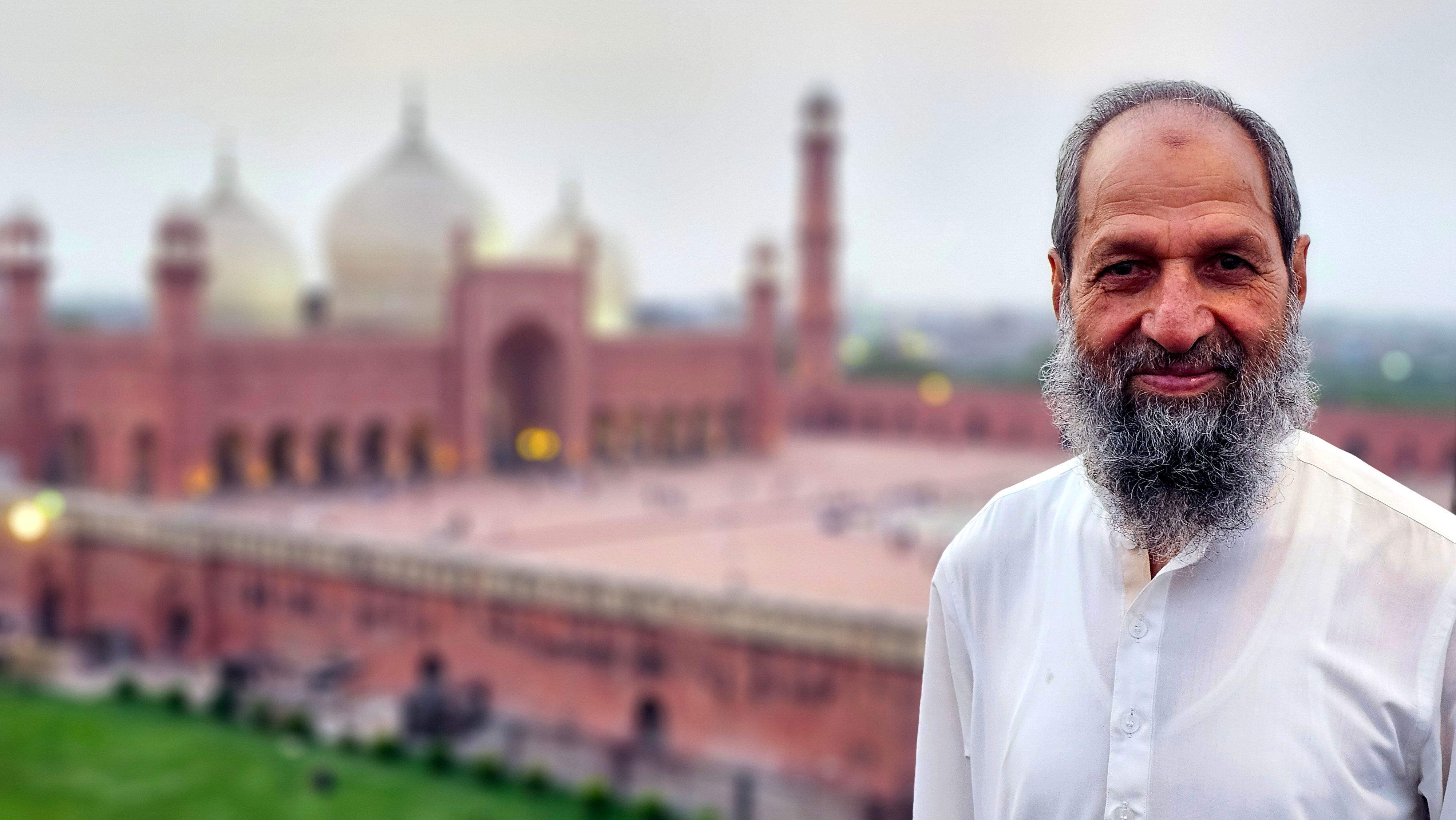 Portrait of an elderly man standing in front of the iconic Badshahi Mosque in Lahore.