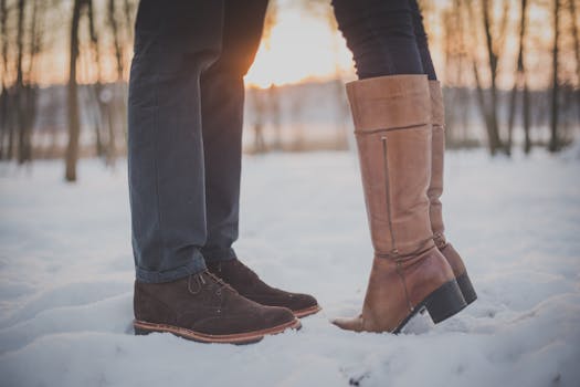 Close-up of couple's boots touching in snowy winter landscape with sunset.