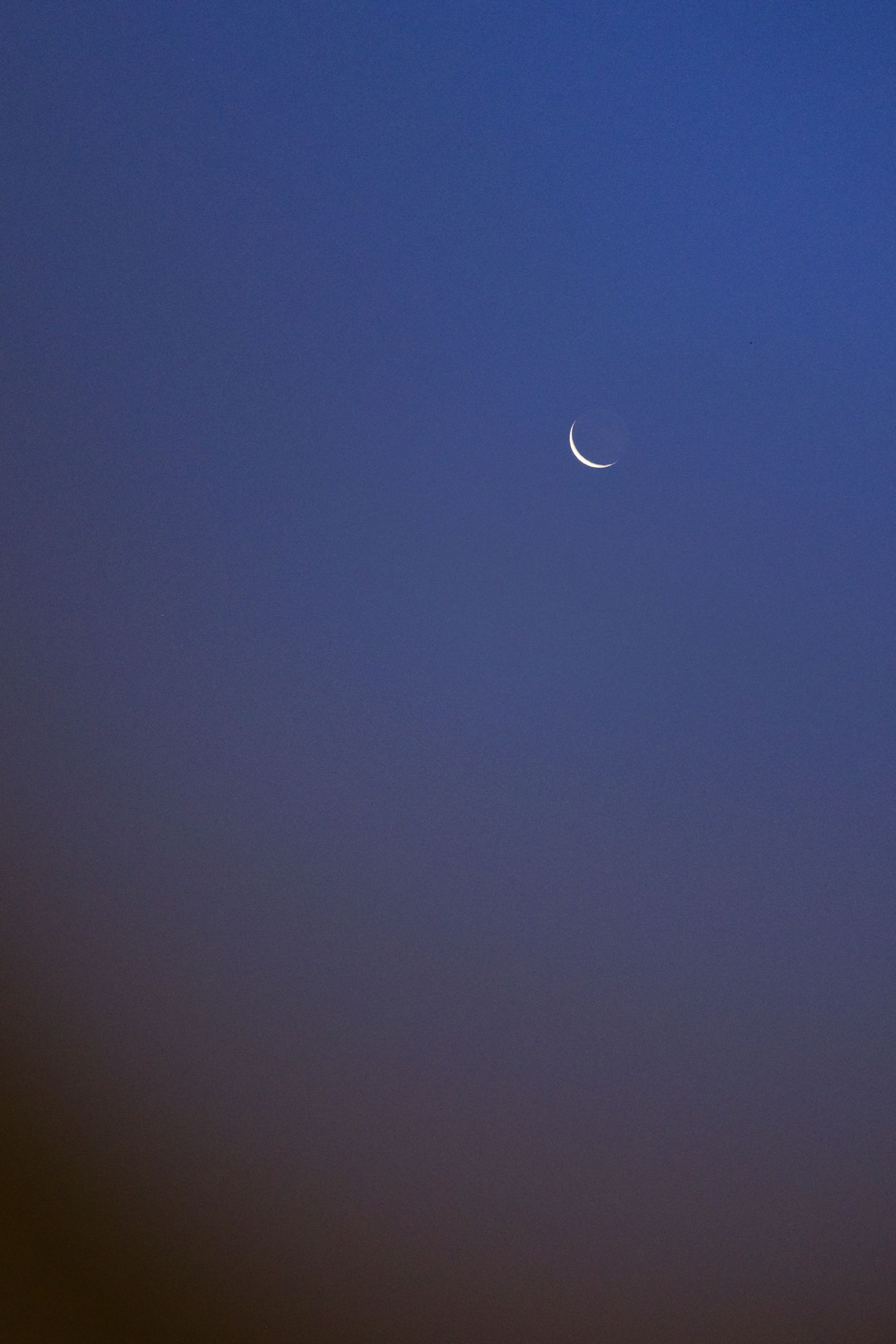 Fin croissant de lune brillant dans un ciel bleu crépusculaire vertical