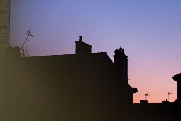 Silhouettes de toits et d'antennes télé sur un ciel pastel au crépuscule