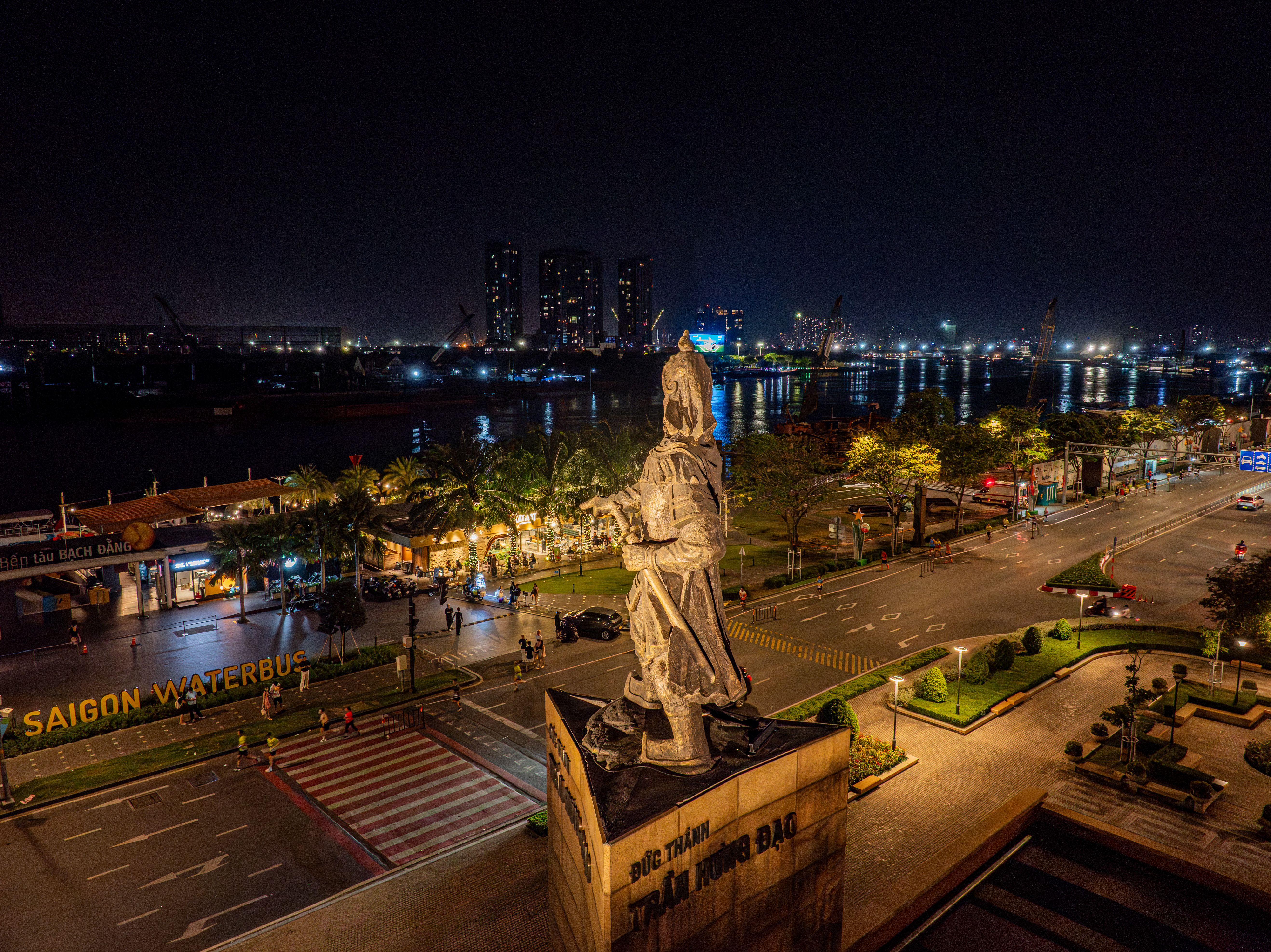 Night view of Saigon riverfront with Trần Hưng Đạo statue and city lights.