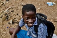 A happy boy in school uniform and backpack, smiling outdoors.