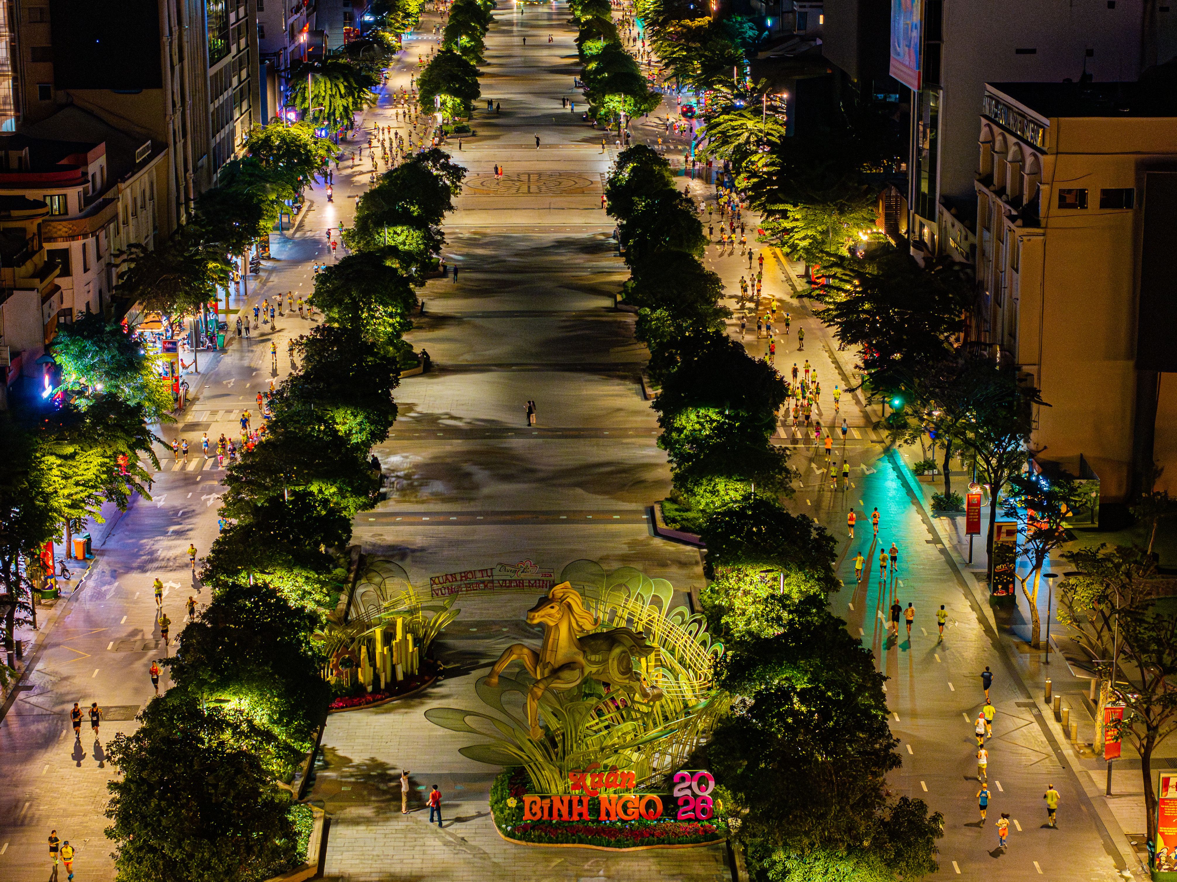 Aerial night view of a bustling city boulevard with colorful lights and people walking.
