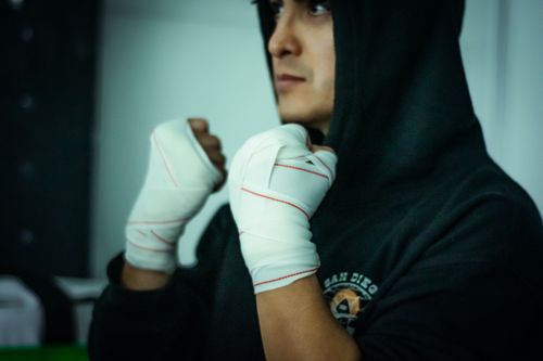 Free A determined boxer in a hoodie with wrapped fists, preparing for a workout indoors. Stock Photo