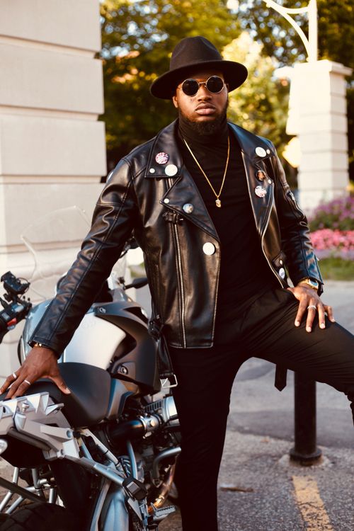 Free Serious young bearded African American male in total black outfit hat and sunglasses standing near modern motorbike against green park Stock Photo