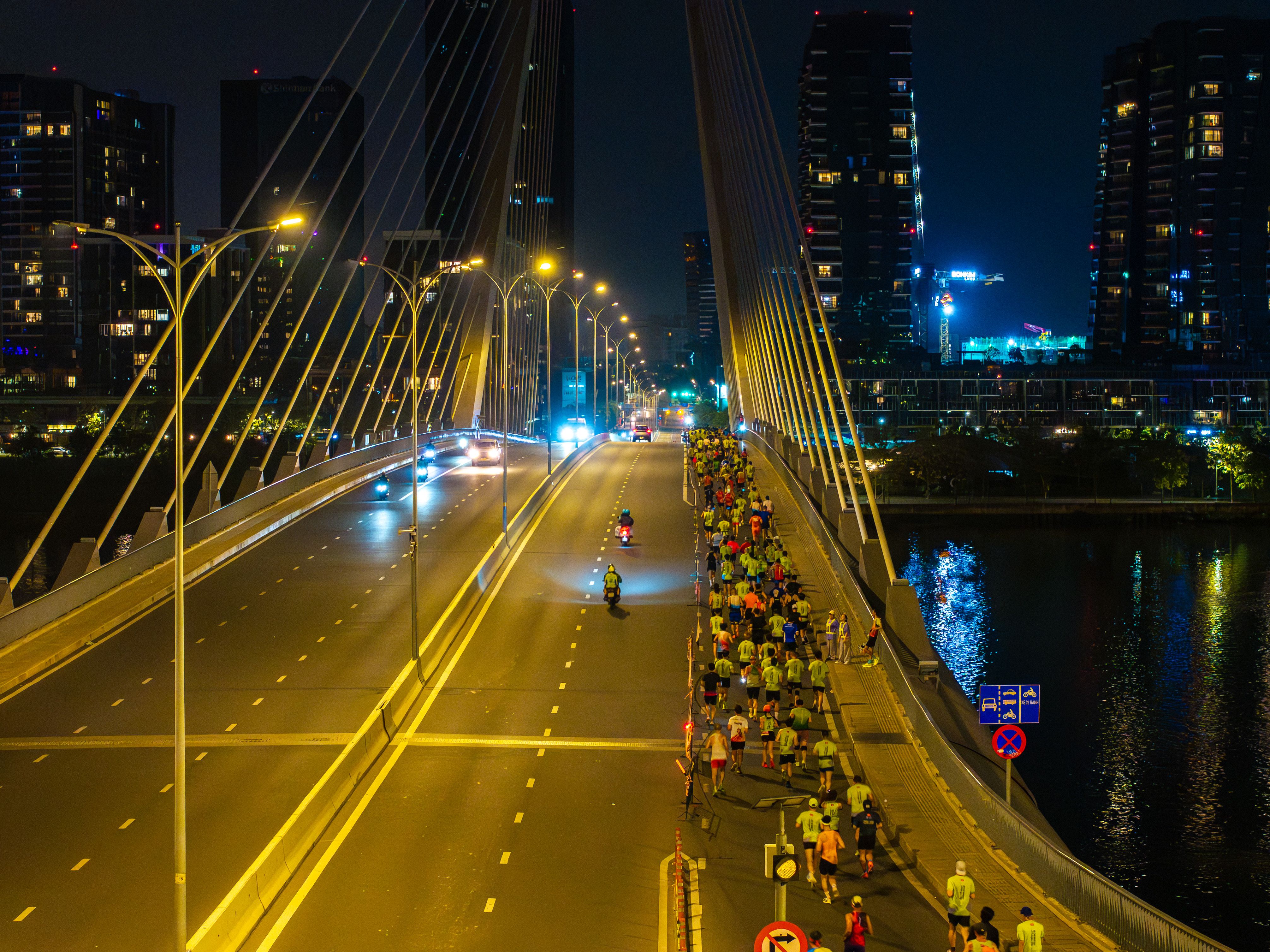 A vibrant night marathon takes place on a city bridge, illuminated by streetlights.