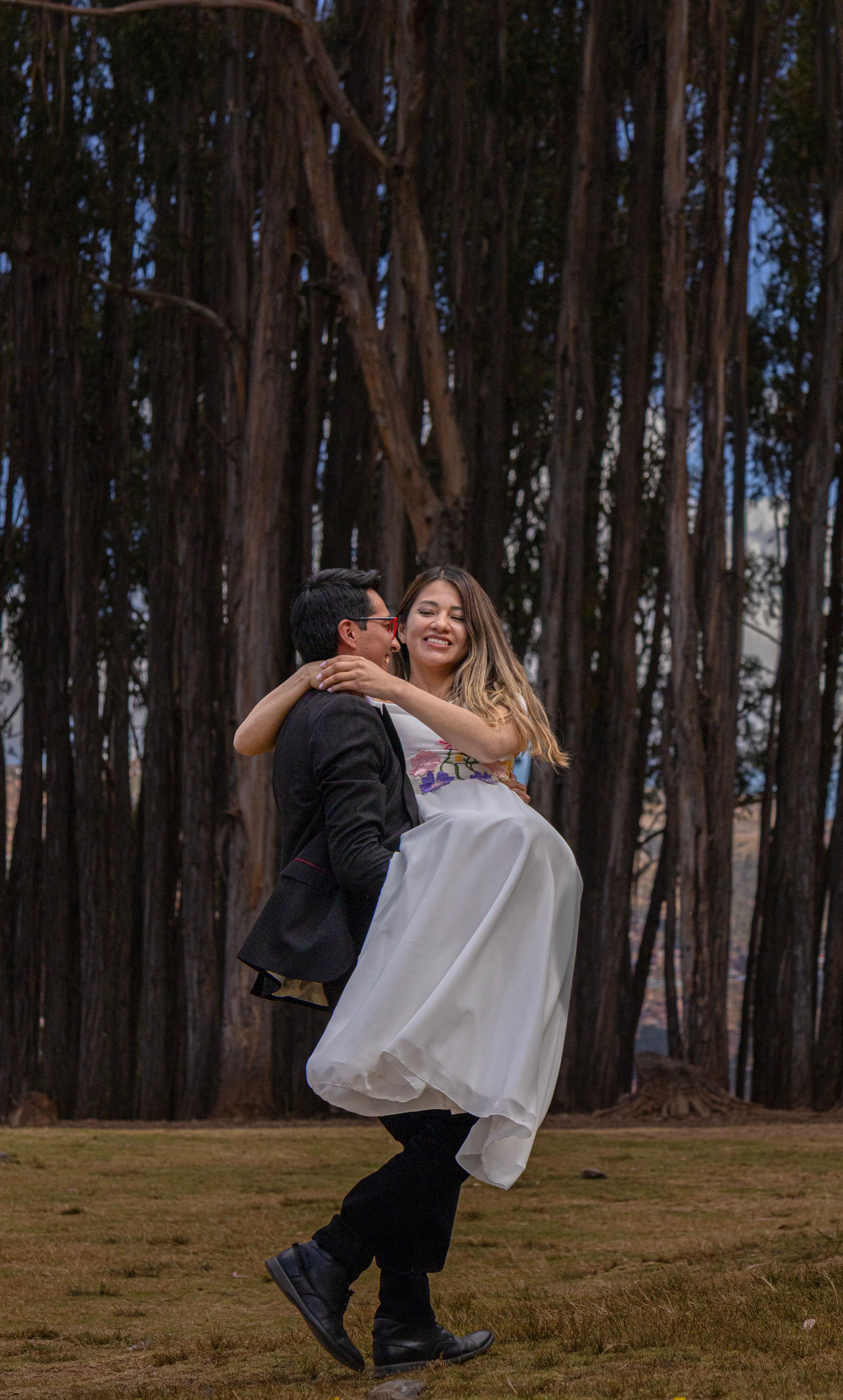 A joyful couple celebrating love outdoors against a backdrop of towering trees.