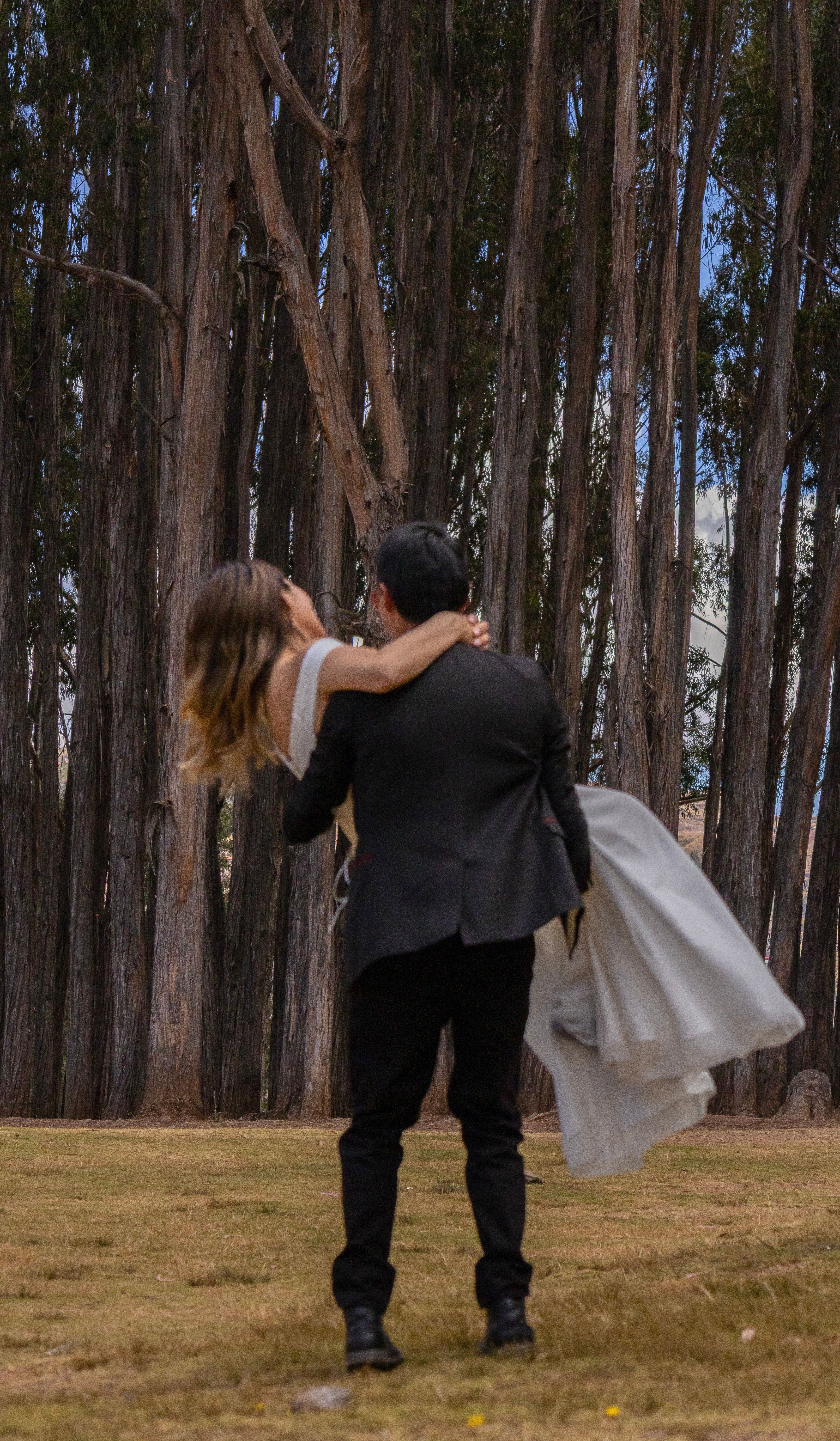 Bride and groom embrace in scenic forest setting. Modern outdoor wedding portrait.