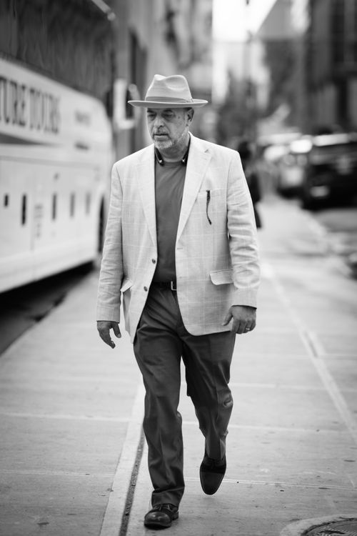 Free An elegant man walks down a city street, dressed smartly with a fedora and blazer, embodying urban sophistication. Stock Photo