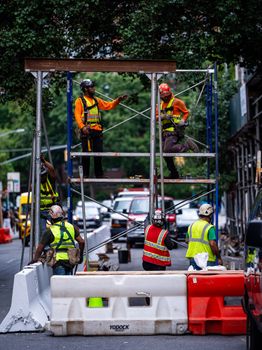 Construction workers actively building scaffolding on a busy city street corner.