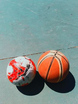 Soccer and basketball on an outdoor court under bright sunlight.