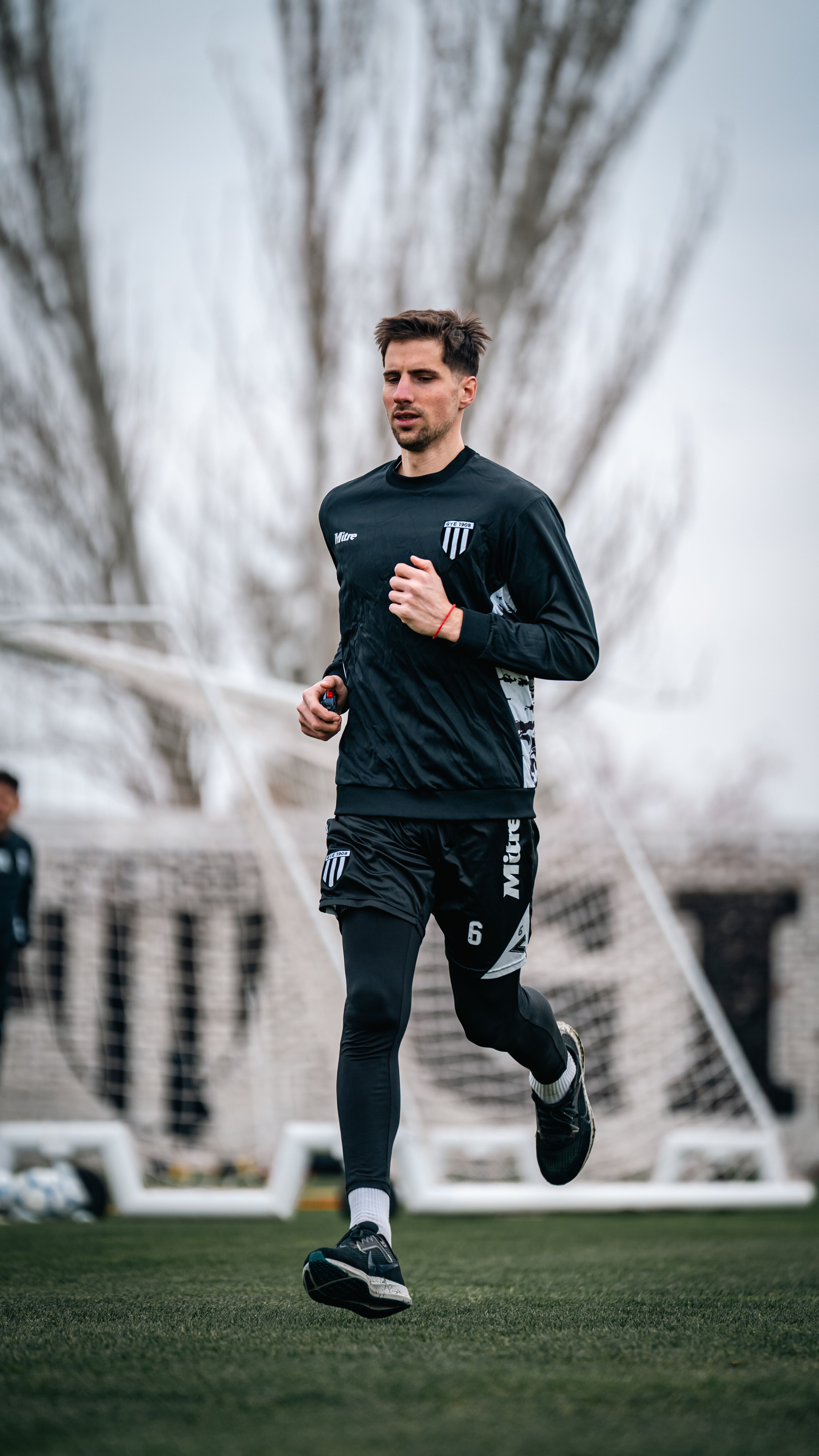Athlete running on a sports field with goalposts in the background, focused on fitness and training.