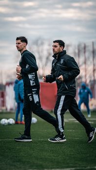 Two soccer players warm up on a field, preparing for a practice session under a cloudy sky.
