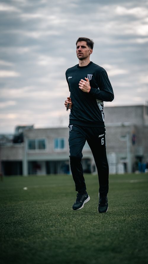 Free A focused athlete jogs on a sports field under a cloudy sky, showcasing determination and fitness. Stock Photo