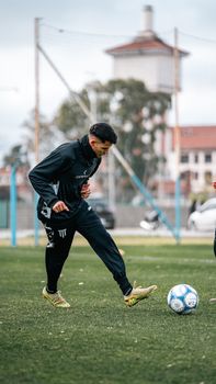 Young adult male practicing soccer on an outdoor urban field, showcasing athletic skills.