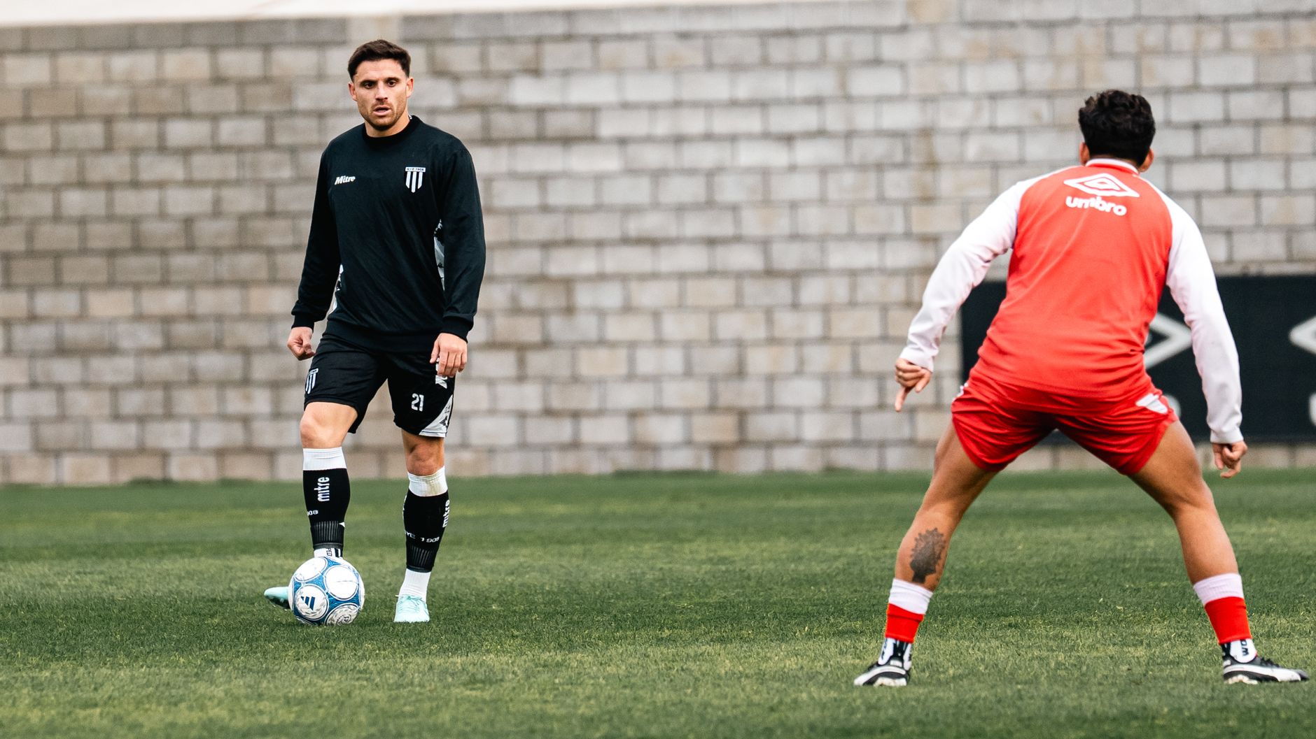 Two football teammates practicing body feints and quick direction changes beside a marked penalty area