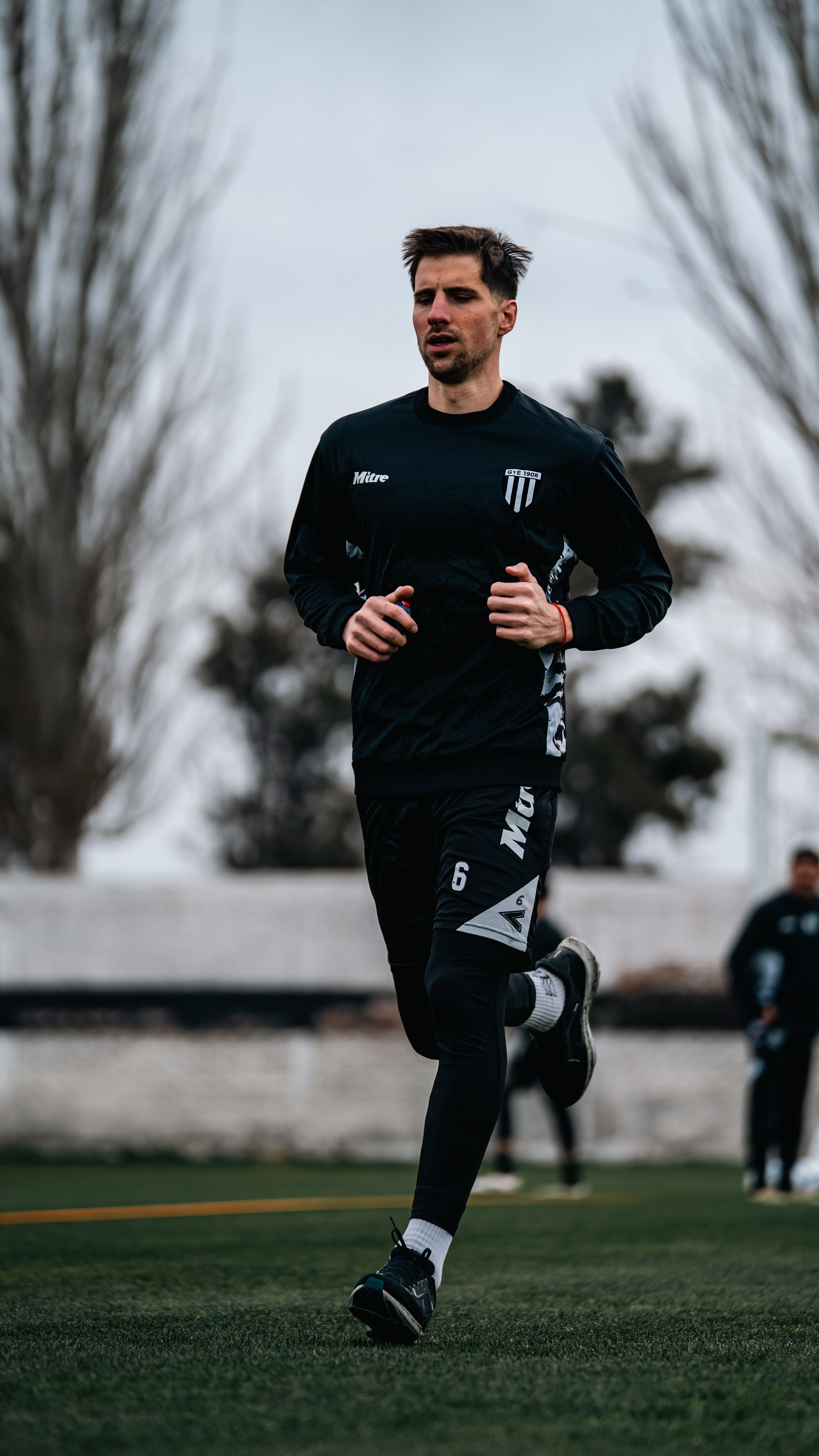 Fotomural Un atleta masculino con ropa deportiva corriendo en un campo de hierba durante el día.