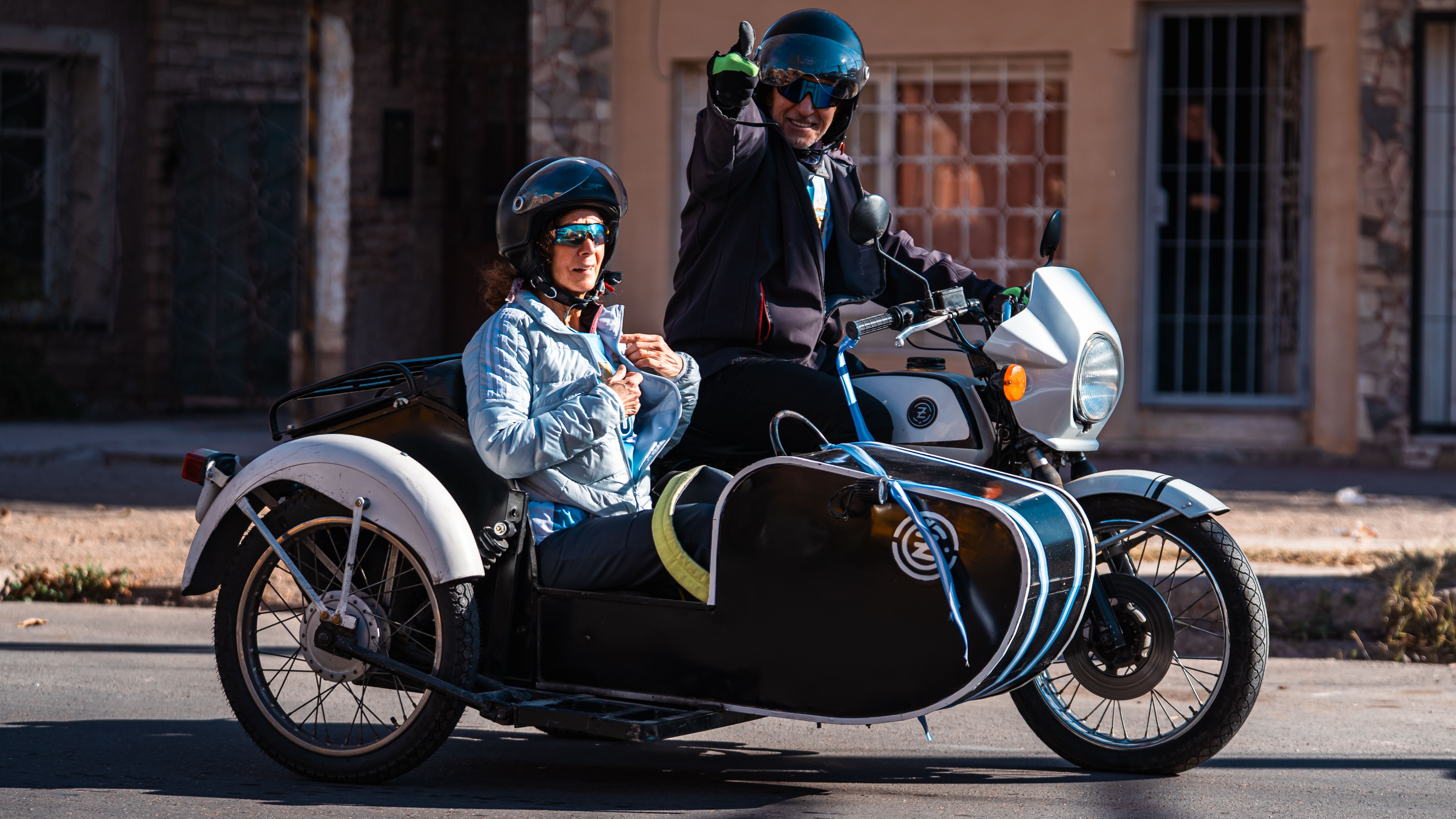 A couple enjoying a ride on a classic motorcycle with sidecar on a sunny day. Safety gear is worn.