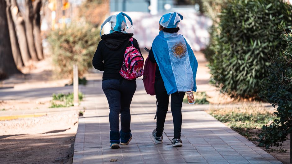 Dos personas con la bandera argentina y sombreros caminando por un camino de la ciudad. Orgullo nacional.