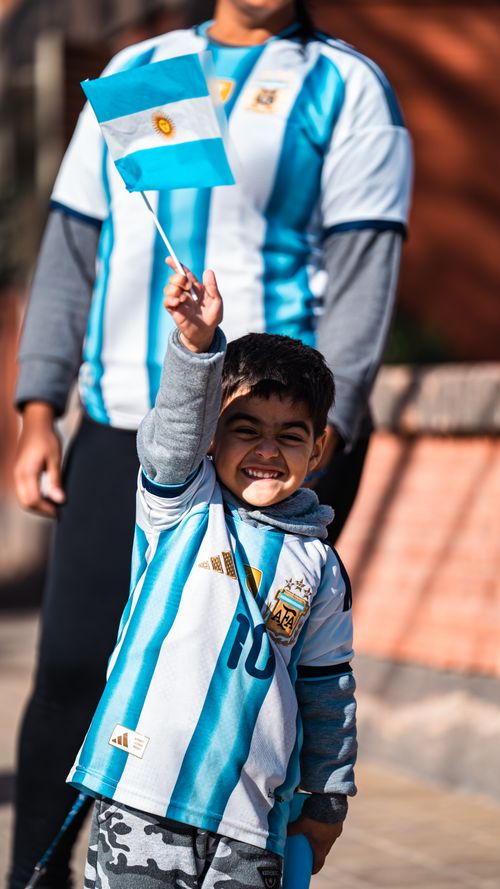 Free A joyful child waving an Argentina flag in team jersey outdoors. Stock Photo