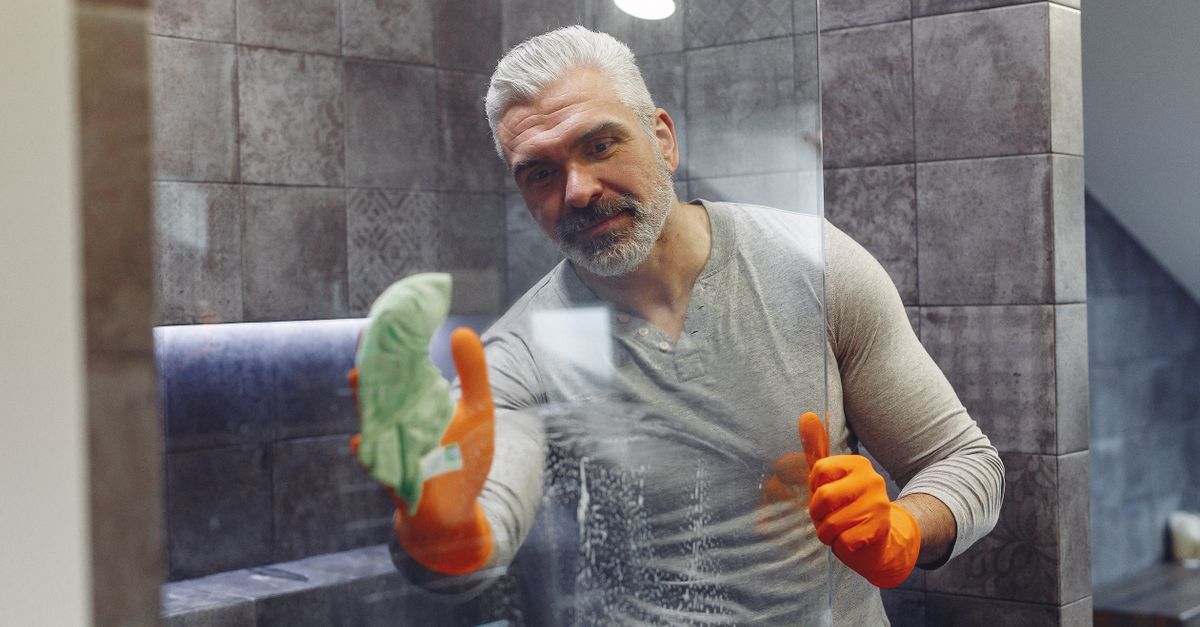Persoon die een glazen douchewand droogtrekt met een douchewisser